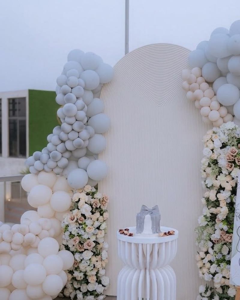 Birthday setup with a white and grey balloon arch, floral columns and a cake plinth by Wedding Alley