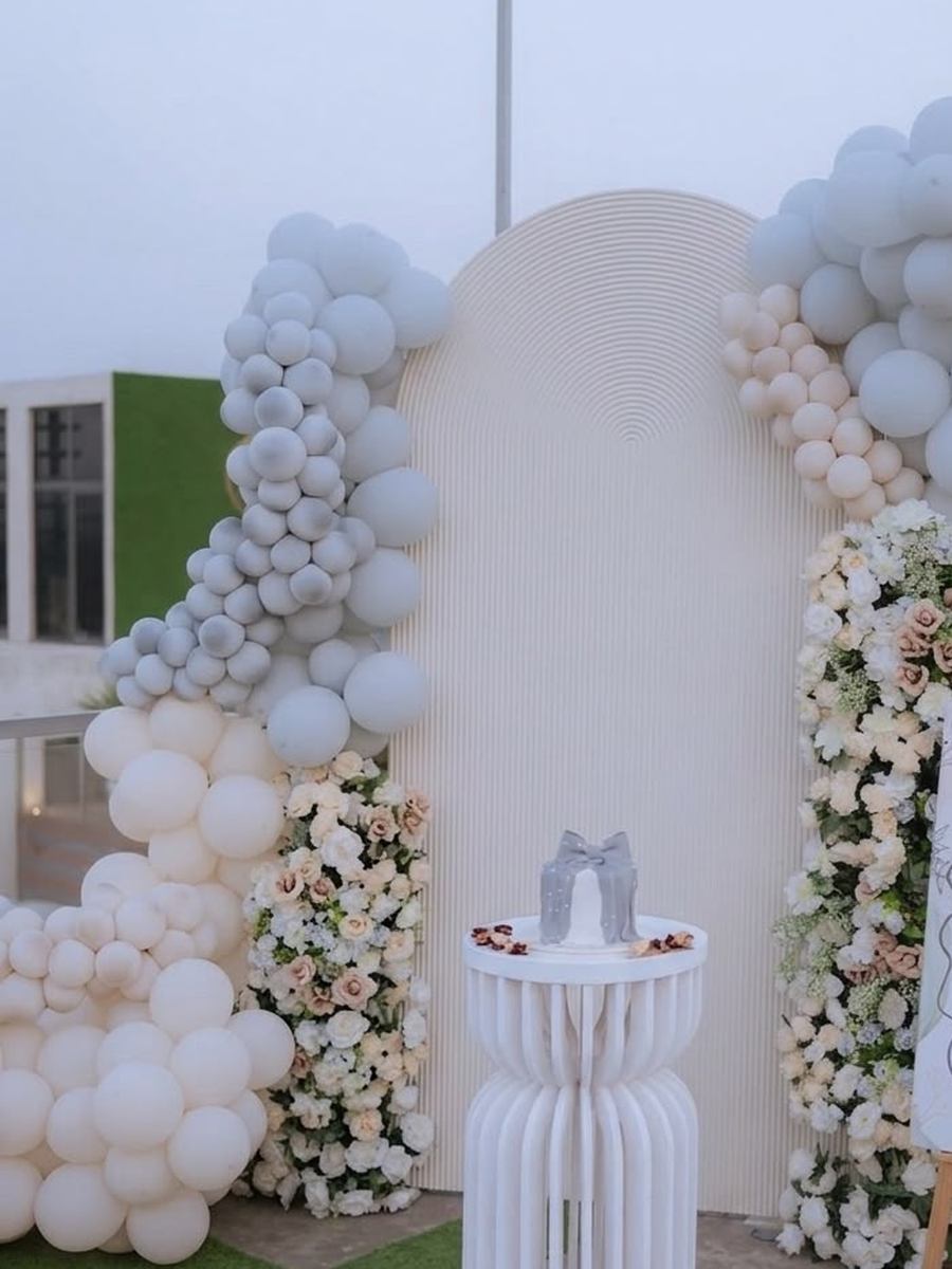 Birthday setup with a white and grey balloon arch, floral columns and a cake plinth by Wedding Alley